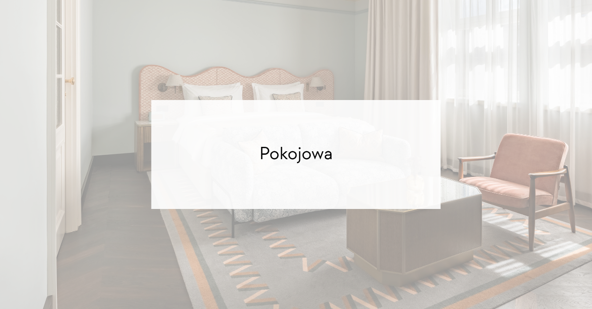 Hotel bedroom with a peach upholstered headboard, white bedding, nightstands, a pink armchair, glass coffee table, and a geometric rug.