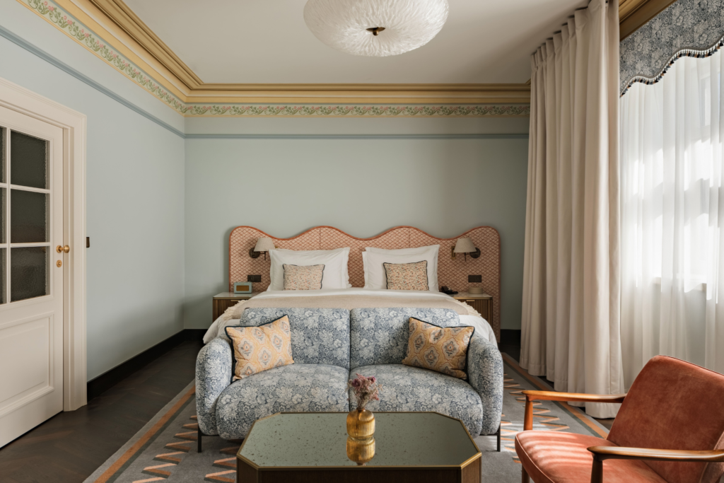 Projekt bez nazwy 2 - Hotel Kraków – Stradom House Hotel&Spa ★★★★★ Elegant hotel bedroom with a pale blue wall, a curved upholstered headboard, white pillows, and side tables flanking the bed beneath decorative wall trim.
